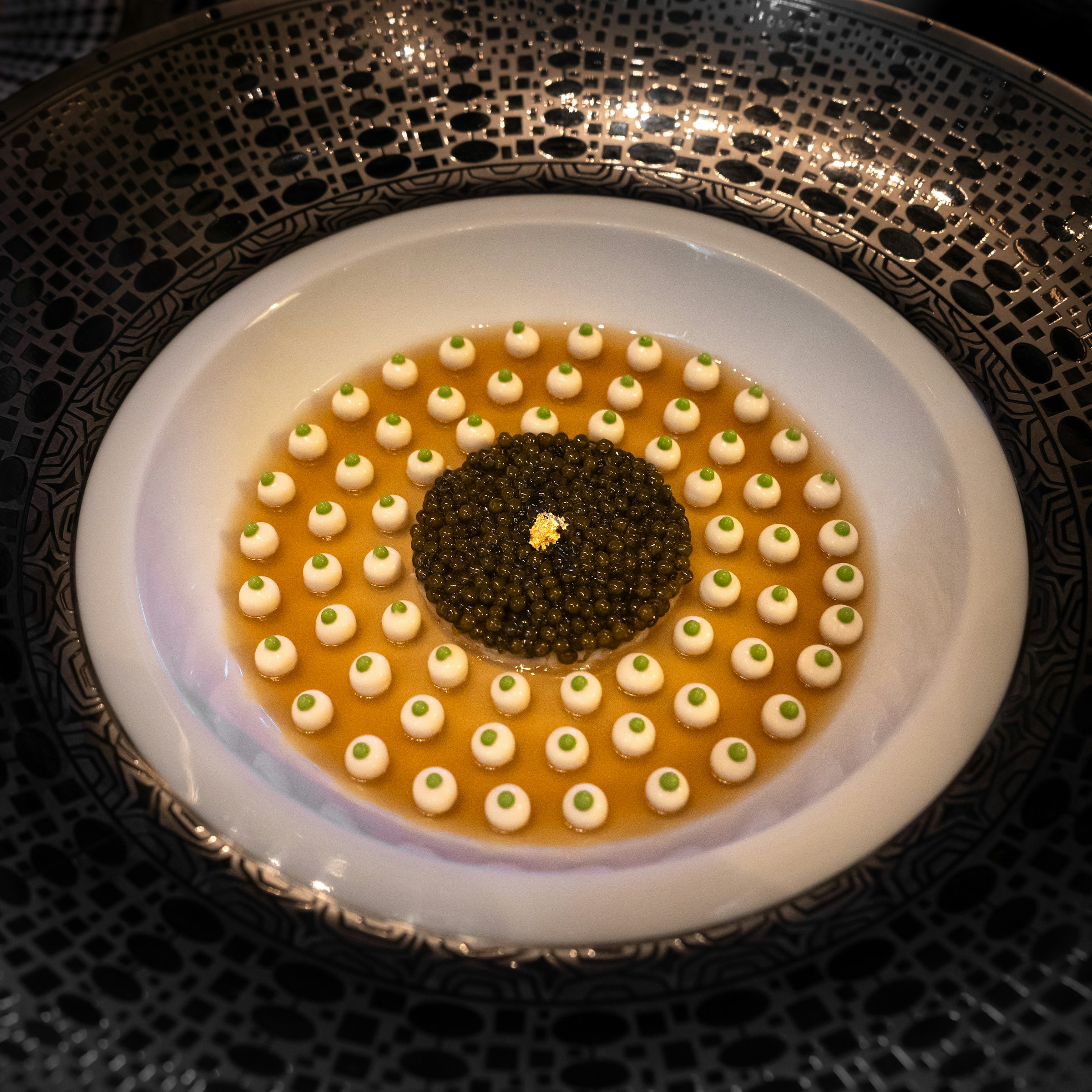 Caviar and pearls of cream on a black plate, seen from above