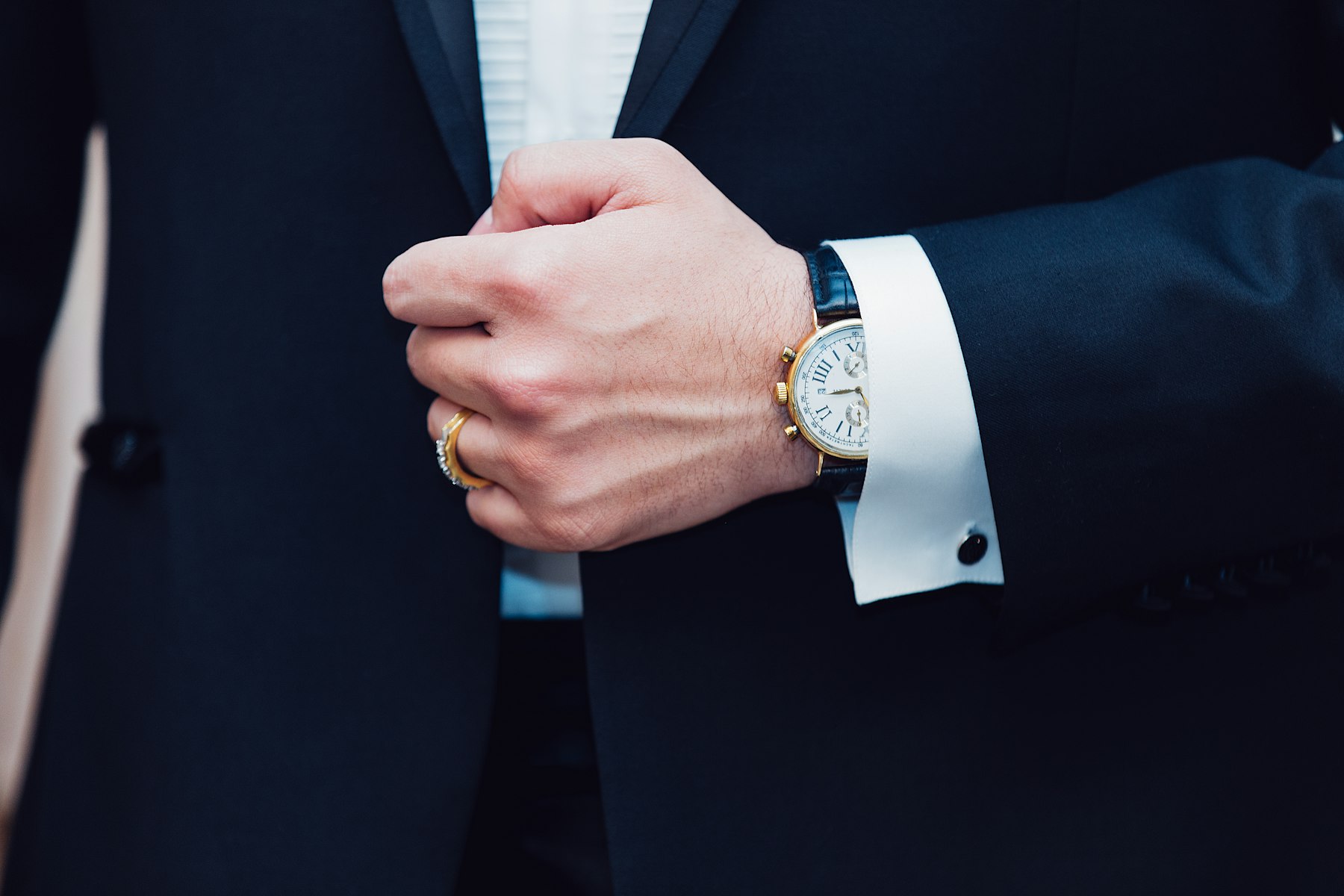 A member in a dark suit adjusting his cuff and watch