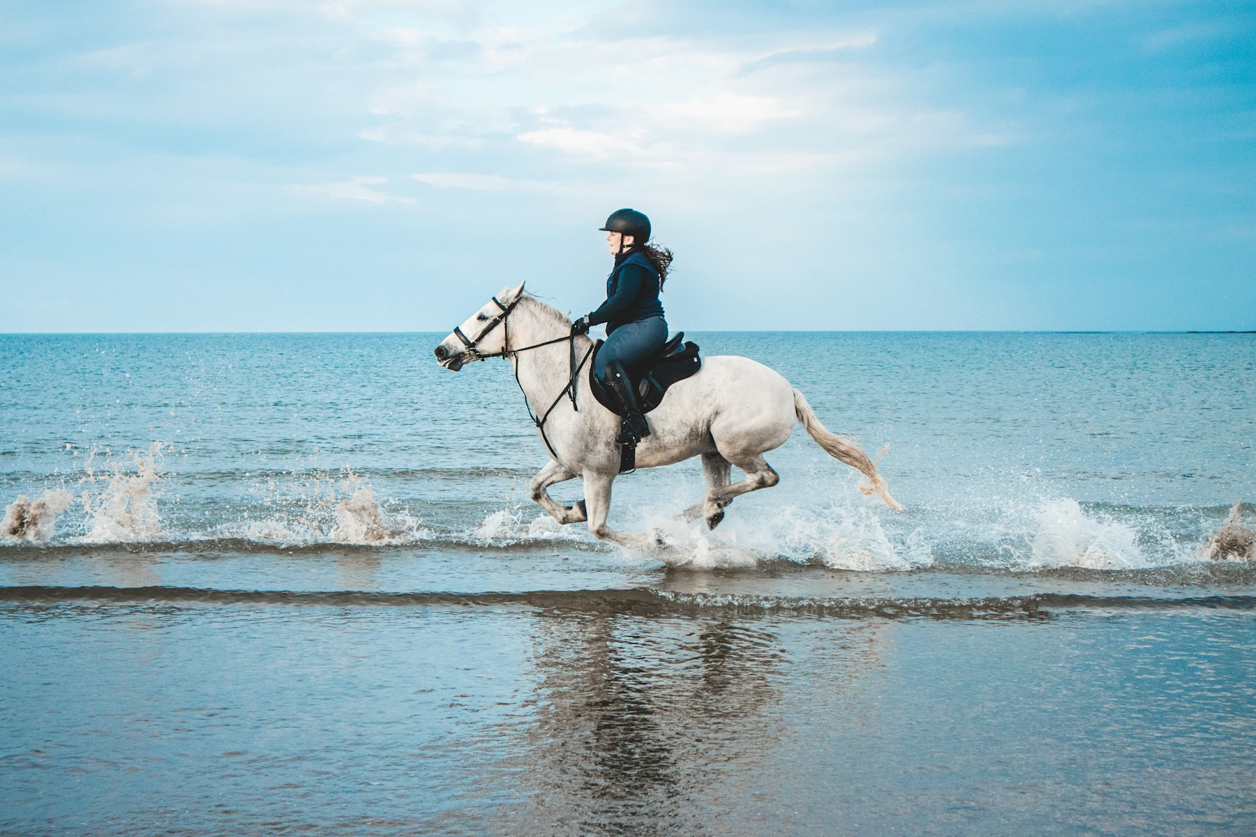 Rider galloping a white horse through the sea
