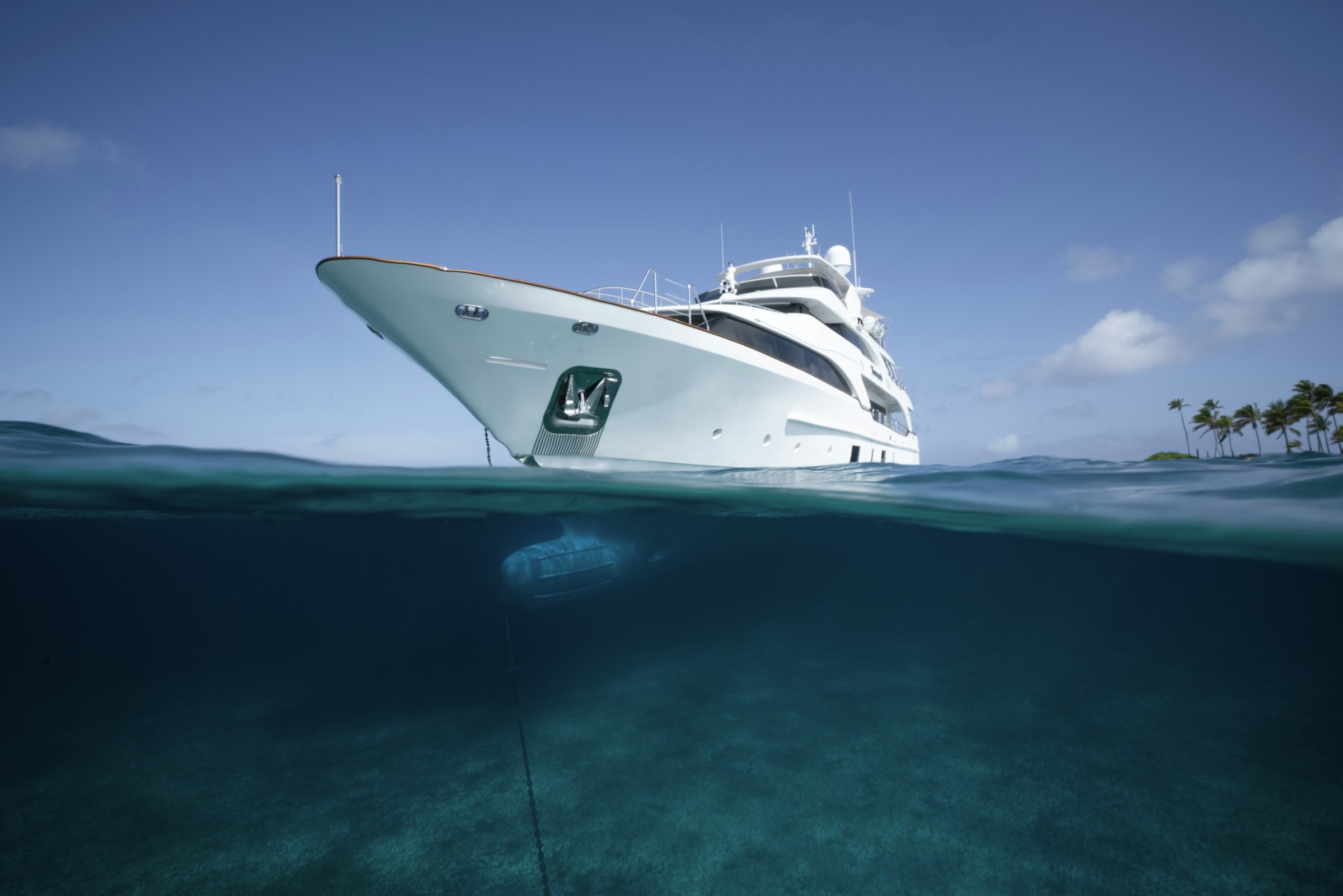 A white superyacht at anchor, seen half above and half below the waterline