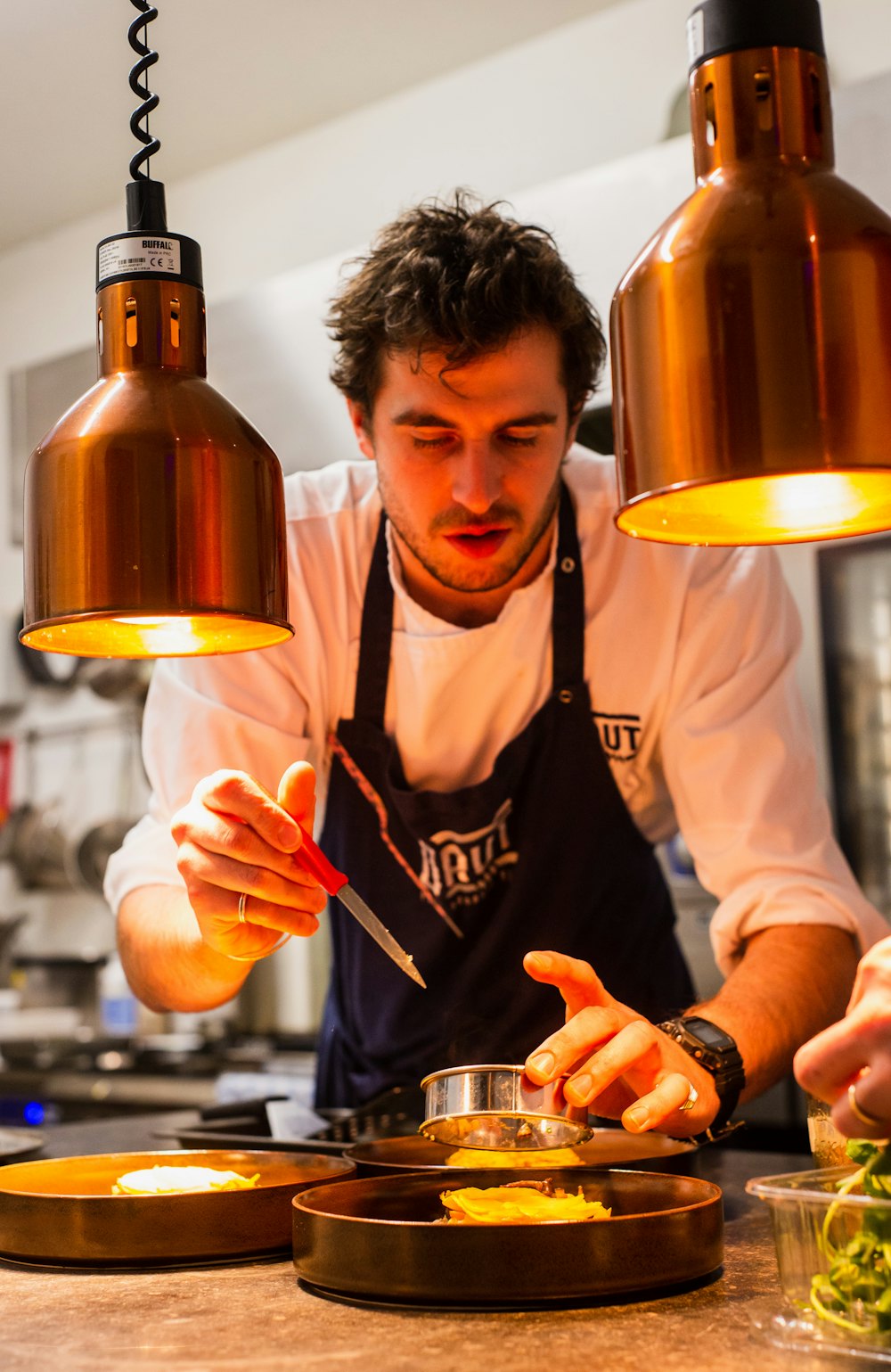 Chef plating a dish under warm lamps