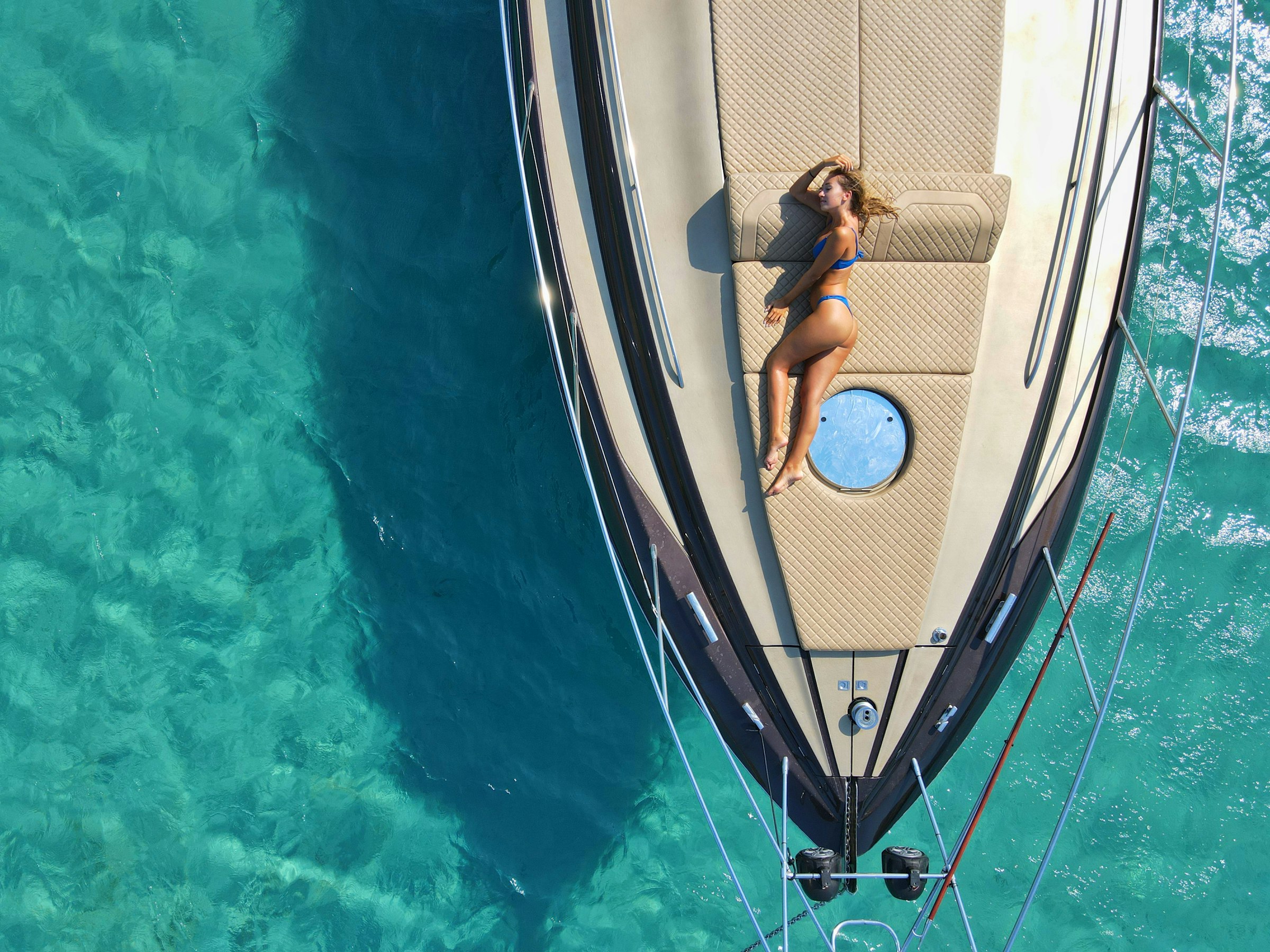 Woman resting on the bow of a yacht over turquoise water